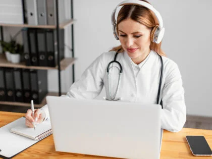 female doctor at laptop wearing headphones and taking notes