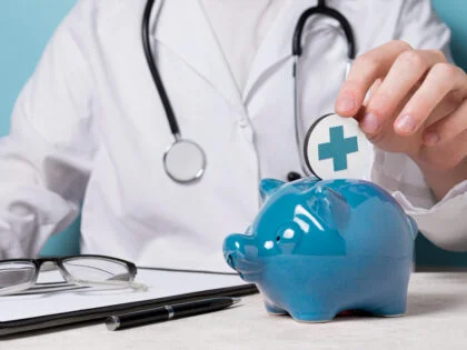 doctor in white coat putting token in to blue piggy bank