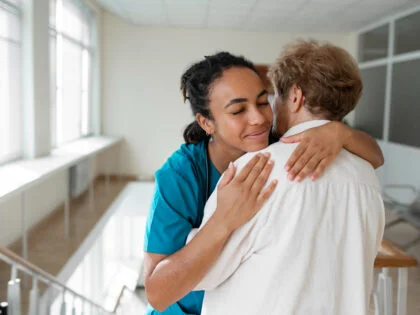 female nurse in blue scrubs hugging patient in white gown