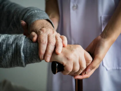 close up of nurse holding old persons hands which are supported on the top of a walking stick