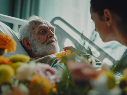 senior patient in hospital bed surrounded by flowers being take care of by nurse