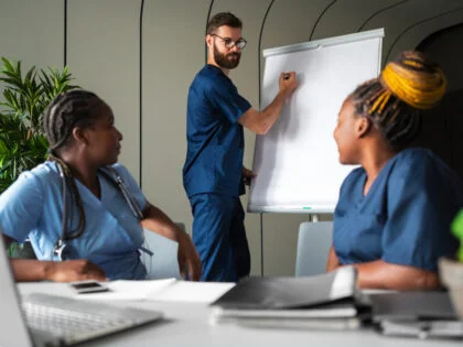 nwo femal nurses and one male nurse in blue scrubs tudying together