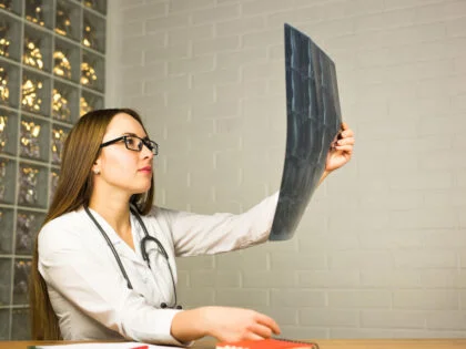 femaile doctor with long hair and glasses studying sheet of xrays