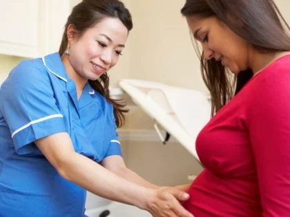 nurse in blue tunic touches the stomach of female patient in red top