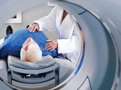 practitioner in white coat standing over patient in blue gown in front of mri scanner