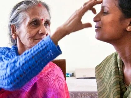 old lady wearing a pink sari touches the forehead of another female