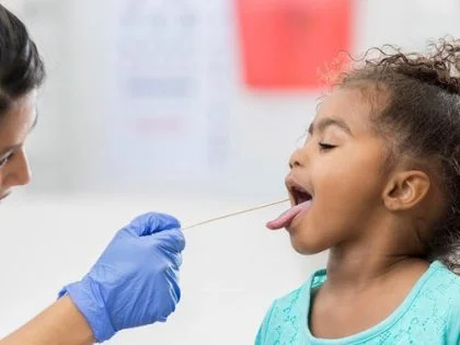 female nurse taking oral swab from young girl while mother looks on