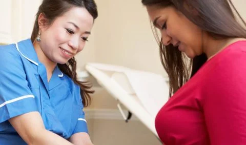 female nurse in blue tunic with white piping with female patient in red top