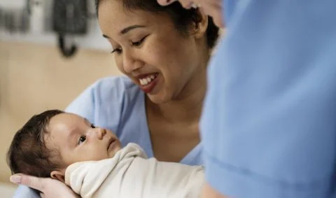 Reducing Avoidable Term Admissions - two females in blue scrubs holding small baby wrapped in white blanket