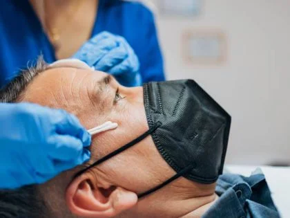 nurse in blue scrubs taking swab from patient's face who is wearing a black mask