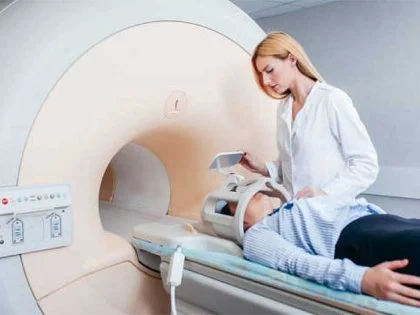 female practitioner in white coat operates an mri scanner for male patient in blue shirt and trousers