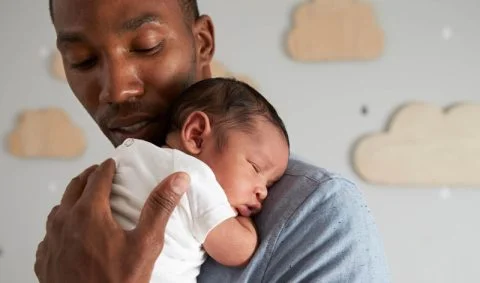 Man holds small baby over his shoulder infront of wall decorated with clouds