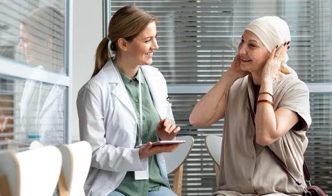 female doctor in white coat holding electronic tablet talking to woman patient in windowed room