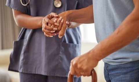 female nurse in grey scrubs helps male patient with walking stick