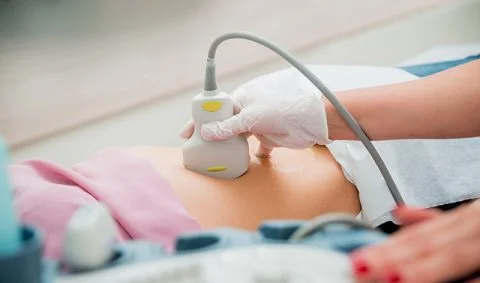 white cloved hand holding ultrasound to a patient;'s stomach