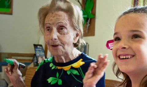 Dementia course - elderly lady holding green pen sits next to smiling girl