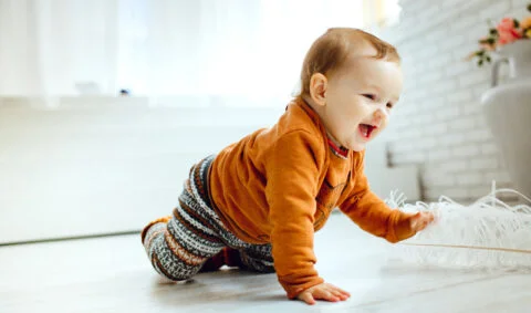 Healthy child suite programme course - happy baby in orange top and patterned trousers crawls across the floor of a bright room