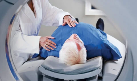 irmer ionising radiation regulations course - practitioner in white coat standing over patient in blue gown in front of mri scanner