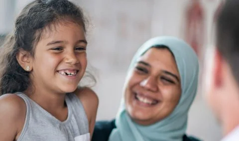 smiling woman in hijab next to smiling girl in front of male doctor