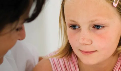 female in white coat comforting girl in pink top