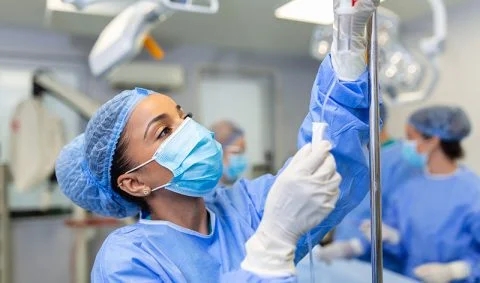 female medic wearing blue scrubs and a head covering sets up an IV in a medical setting