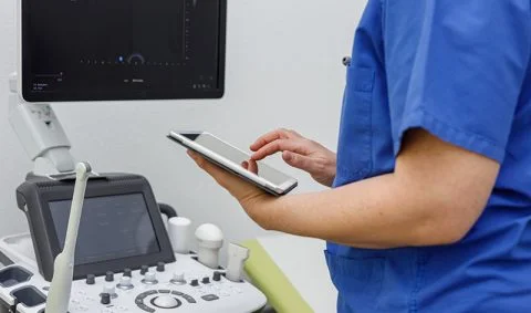 healthcre professional in blue scrubs using digital tablet in front of a medical scanner