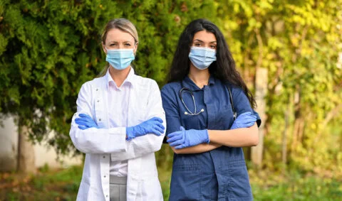 two female medics wearing masks one is in a white coat and the other in a blue coat