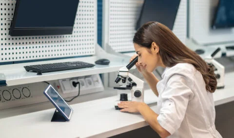 Medical Examiner - woman in white lab coat looks into microscope