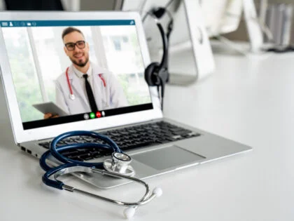 A laptop displaying elearning with a doctor, featuring a stethoscope and headset on the desk in front of the laptop.