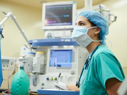 female anesthetist in green scrubs and blue hat working in operating theatre